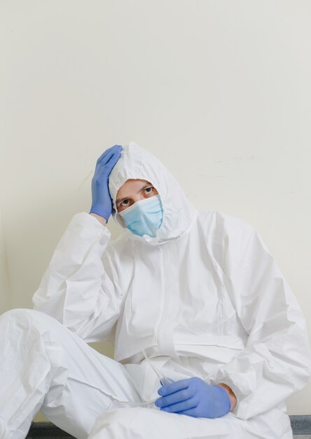 Un médico triste con un traje protector está sentado en el suelo del pasillo del hospital. Trabajadores de la salud durante la pandemia del coronavirus Covid19.