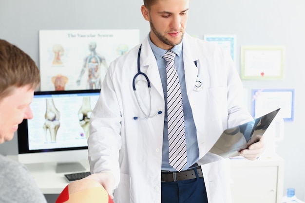 El médico usa uniforme y examina la rodilla del hombre