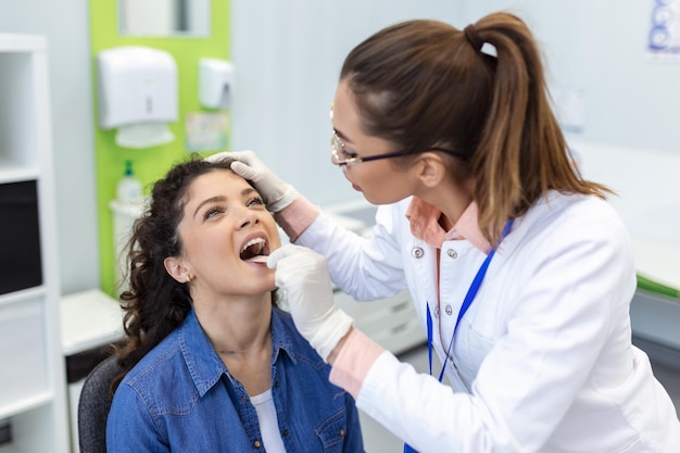 Médico usando una espátula de inspección para examinar la garganta del paciente Médico de ORL haciendo un examen de garganta de una mujer paciente abrió la boca para un chequeo de garganта