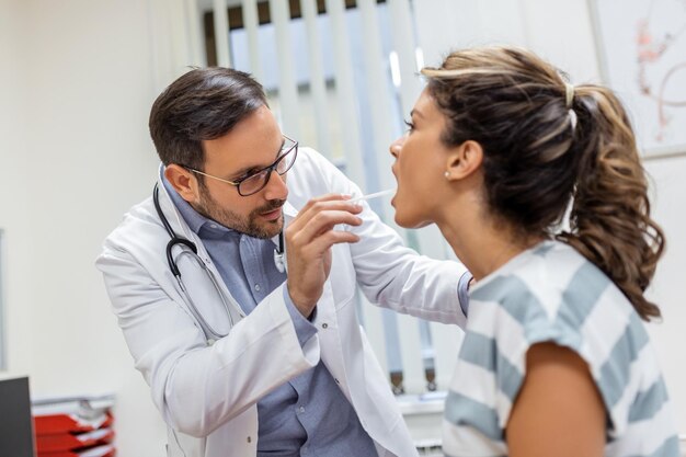 Médico usando una espátula de inspección para examinar la garganta del paciente Médico de ORL haciendo un examen de garganta de una mujer paciente abrió la boca para un chequeo de garganта