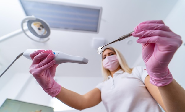 Médico usando máscara cirúrgica rosa no rosto. Dentista em protetor esfrega no escritório de odontologia com instrumentos mrdical nas mãos. Vista dos olhos de um paciente.