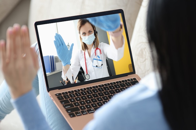 Médico usando máscara e luvas, comunicando-se com o paciente via laptop. Conceito de telemedicina
