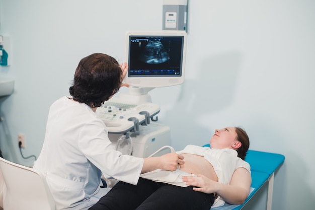 Médico utilizando ultrasonido y cribado del estómago de la mujer embarazada.