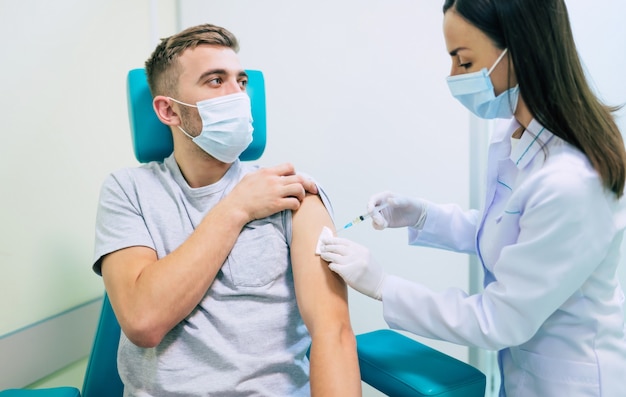 Médico de la vacuna de Covid-19 o coronavirus sosteniendo una jeringa y usando algodón antes de inyectar al paciente en la máscara médica.