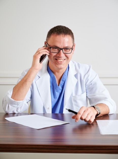 Médico varón alegre hablando por teléfono móvil en el trabajo