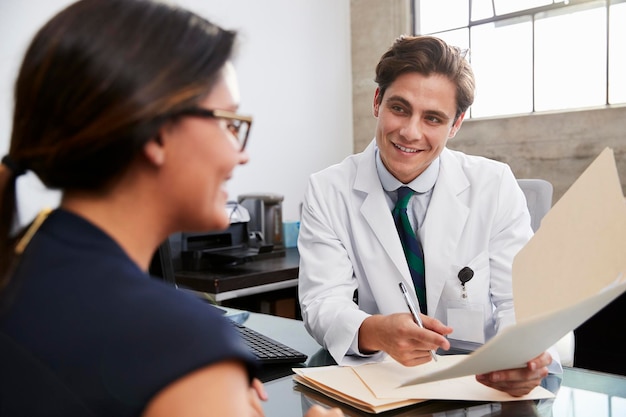 Médico varón blanco que muestra el archivo a una paciente en el consultorio