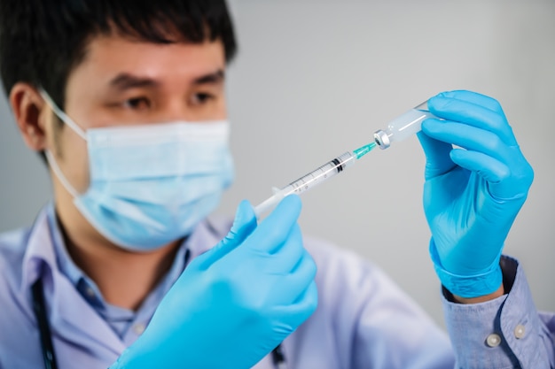 Médico varón dibujando la botella de la vacuna en la jeringa de medicina de inyección