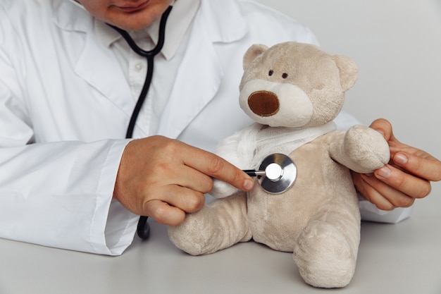 Médico varón con estetoscopio y oso de peluche en consultorio médico