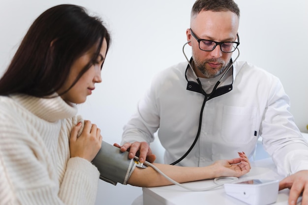 El médico varón en el examen médico mide la presión arterial de una paciente mujer. Mujer con cita en cardiólogo