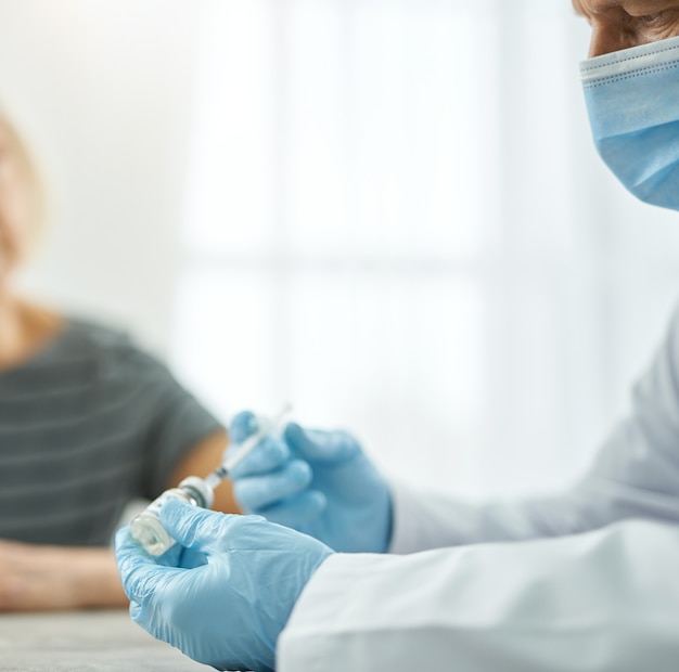 Médico varón en guantes estériles llenando la jeringa con vacuna