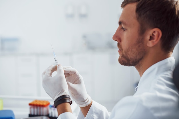 Médico varón con jeringa se está preparando para la toma de muestras de sangre en la sala de la clínica.