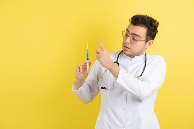 Médico varón joven en bata blanca con jeringa médica.