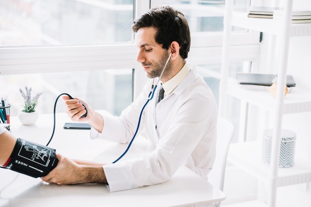 Foto médico varón medir la presión arterial del paciente en la clínica