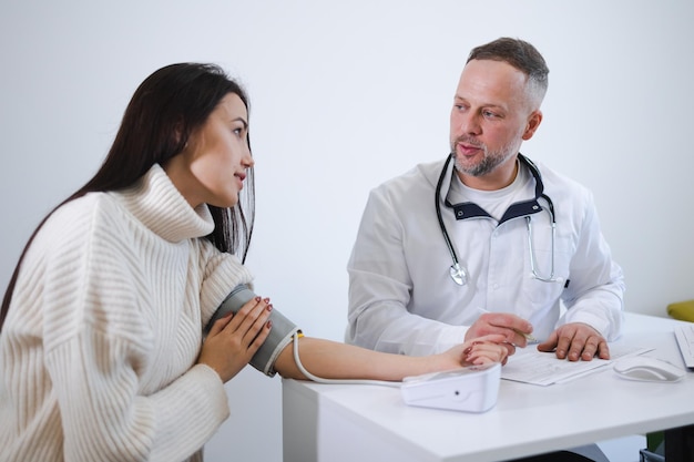 El médico varón mide la presión arterial de la mujer y registra los resultados en la tarjeta del paciente. Mujer en la cita con el cardiólogo