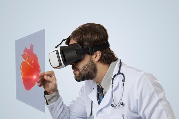 Médico varón en una pared gris con gafas de realidad virtual, mirando un corazón virtual