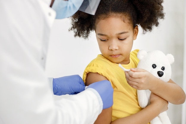 Médico varón pega una curita en el hombro de una niña después de una vacunación