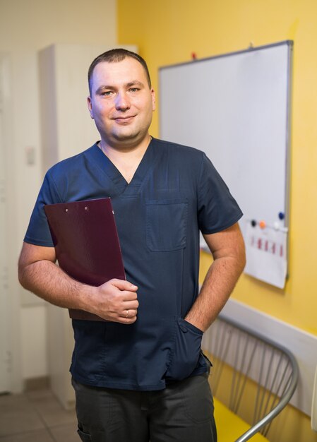 Médico varón de pie con carpeta en el hospital. Pizarra sobre fondo.