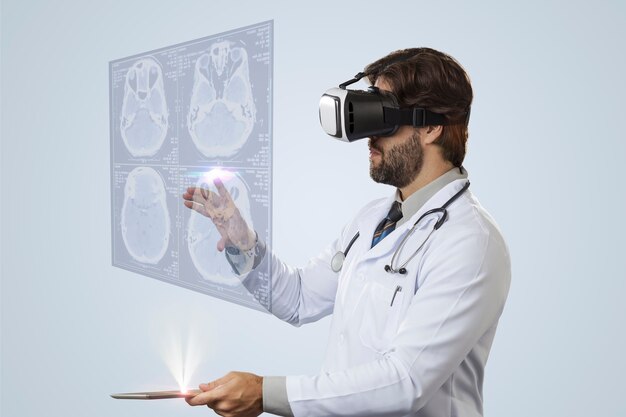 Médico varón sobre una pared gris mirando una pantalla virtual que sale de una tableta