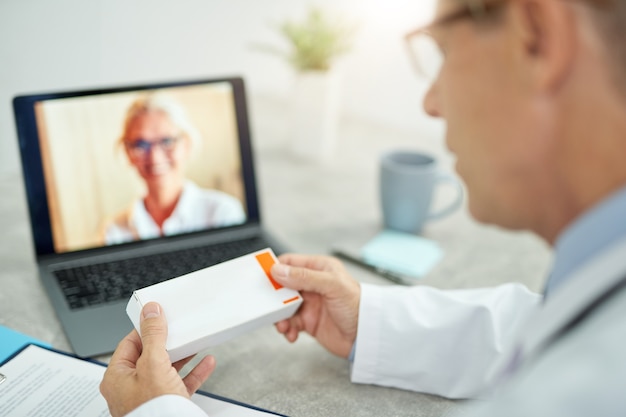 Médico varón sosteniendo medicamentos y usando la computadora portátil en la clínica