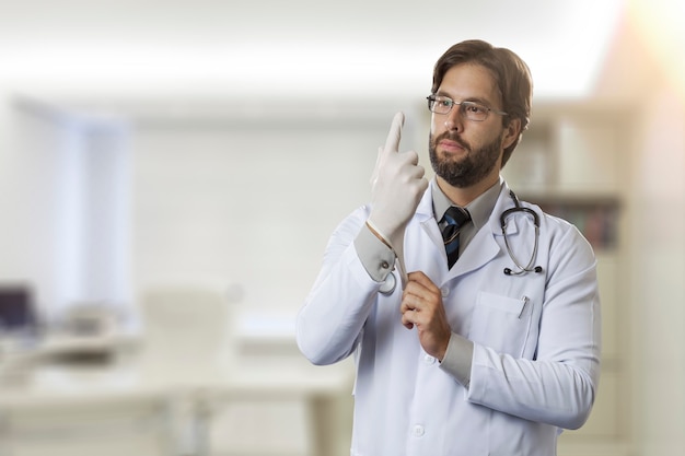 Médico varón en su oficina, poniéndose guantes de látex