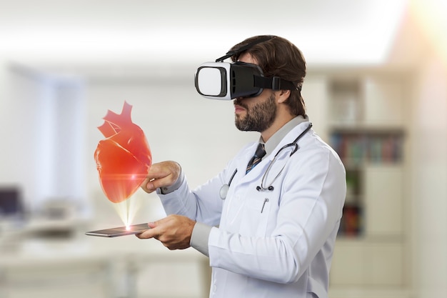 Médico varón en su oficina, utilizando unas gafas de realidad virtual, mirando un corazón virtual