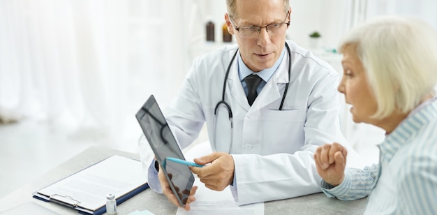 Médico varón con tablet PC y hablando con el paciente en la clínica