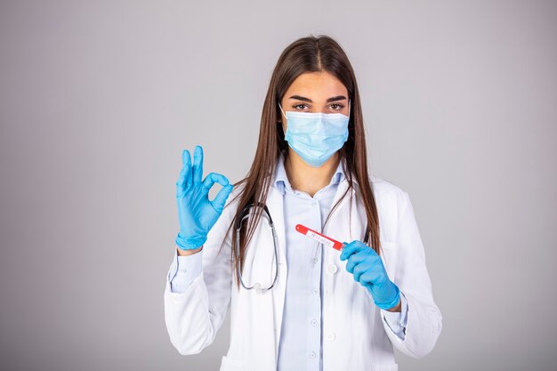 Foto médico vestindo roupa altamente protetora e examinando um novo tubo de ensaio de coronavírus covid 19. enfermeira ou médico com máscara facial segurando exame de sangue com resultado positivo para coronavirus 2019-ncov