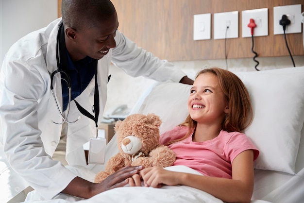 Médico visitando garota deitada na cama de hospital abraçando o ursinho de pelúcia