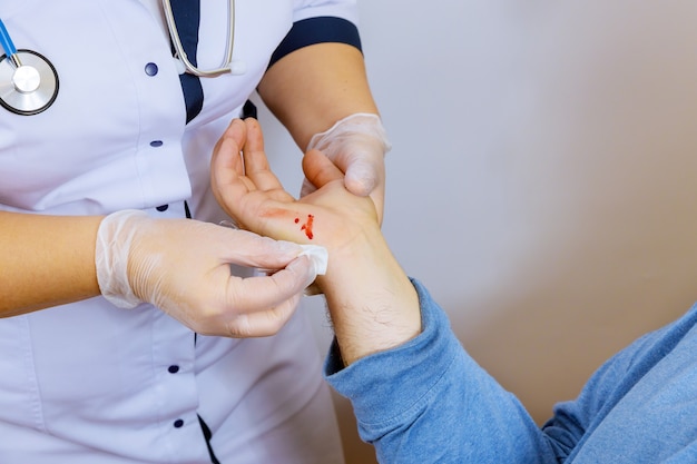 Médico visitante limpia la sangre de la mano lesionada paciente