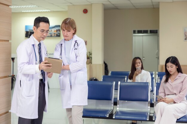 Foto los médicos de asia y occidente sostienen una tableta y conversan sobre un paciente en un hospital.