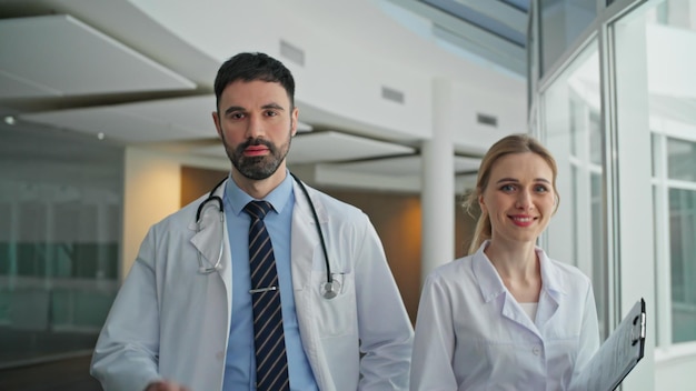 Médicos confiantes a irem ao corredor da clínica. Um homem sorridente a apontar para a câmara.