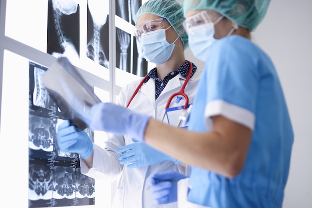 Los médicos en el consultorio médico con máscaras médicas protectoras, guantes y gafas están examinando radiografías.