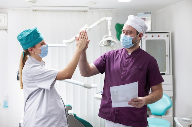 Médicos dentistas masculinos e femininos dando mais cinco enquanto concordam com o tratamento odontológico do paciente