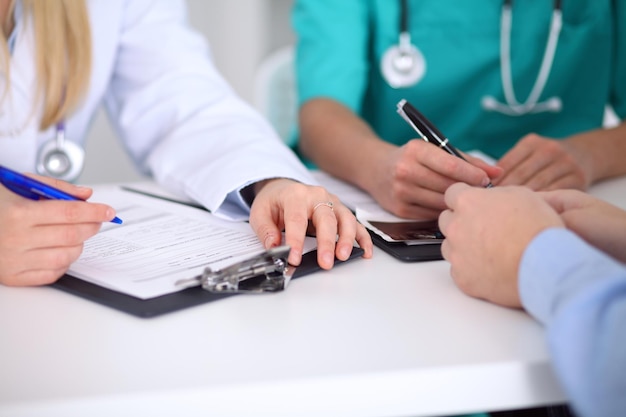 Médicos e pacientes estão discutindo algo, apenas mãos na mesa.