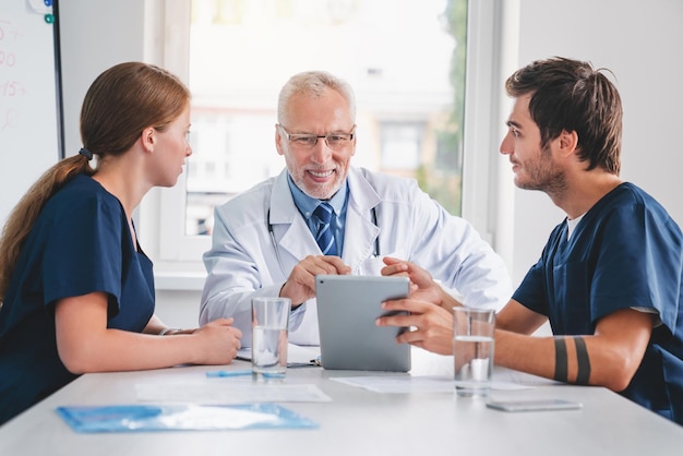 Médicos y enfermeras mirando una tableta digital durante una reunión médica en el hospital