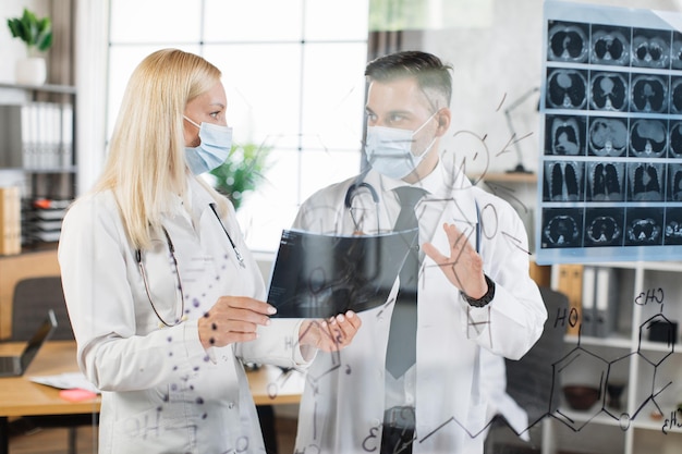 Médicos con máscaras faciales analizando la exploración de rayos x en el hospital