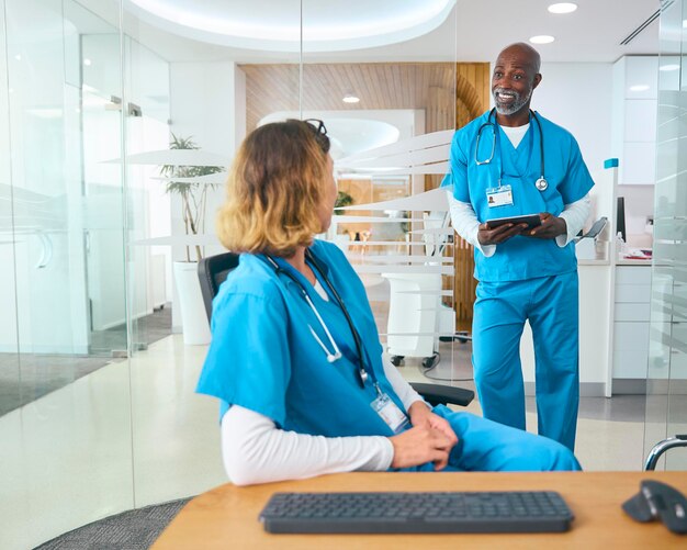 Médicos masculinos e femininos vestindo roupas de cirurgia tendo reunião informal no escritório do hospital