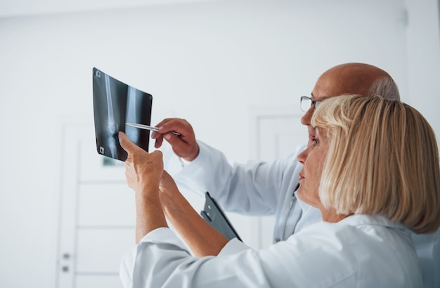 Médicos sêniors e mulheres em uniforme branco examinam o raio-x de pernas humanas.