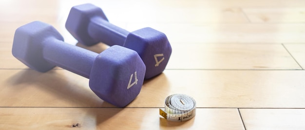 Foto una medida de cinta blanca en un piso de madera dura al lado de dos pequeñas pesas púrpuras dentro de un gimnasio