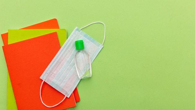 Foto medida de prevenção da propagação do coronavírus na escola máscara cirúrgica, gel de desinfecção com álcool e cadernos em fundo verde