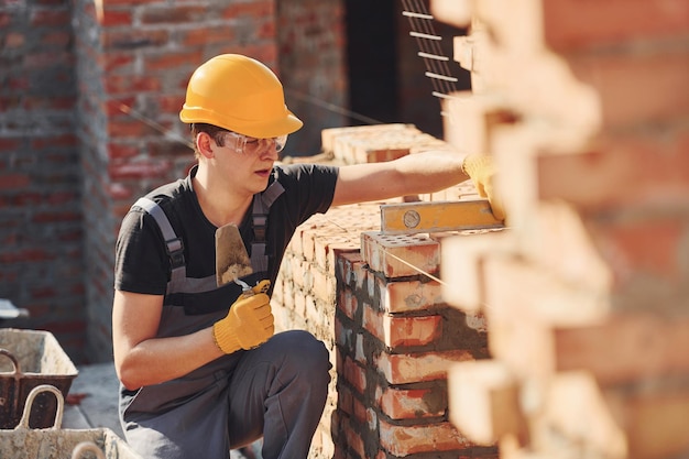 Medidas da parede de tijolos Trabalhador da construção em uniforme e equipamento de segurança tem emprego na construção
