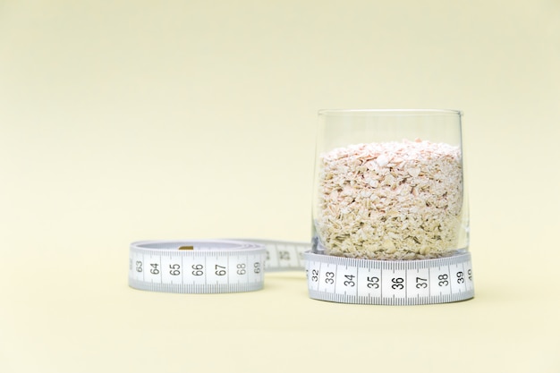 Medidor de medição e copo de flocos de aveia em fundo amarelo. conceito de dieta.