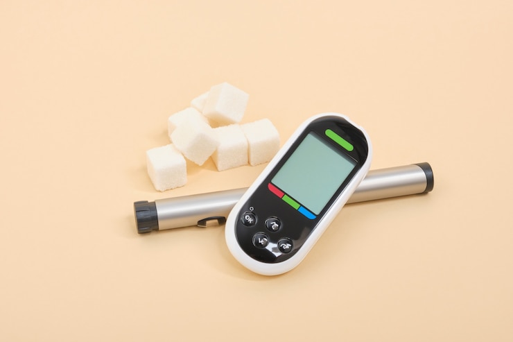 Foto medidor de glucosa negro, pluma de jeringa de insulina y terrones de azúcar blanco sobre fondo beige