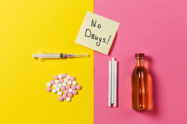 Medikamente bunte Tabletten Pillen abstrakt, leere Spritzennadel, Flaschenalkohol, Zigaretten auf gelbem rosa Rosenhintergrund
