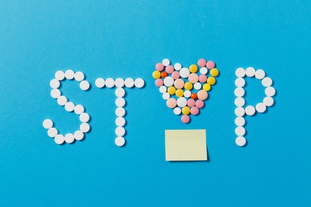 Medikamente weiße, bunte runde Tabletten in Wort Stop auf blauem Hintergrund isoliert