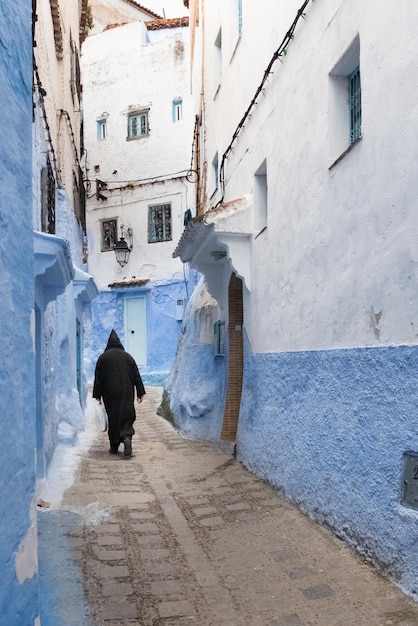 Medina de Chefchaouen em Marrocos Um homem vestido com o tradicional casaco berbere caminha por um beco