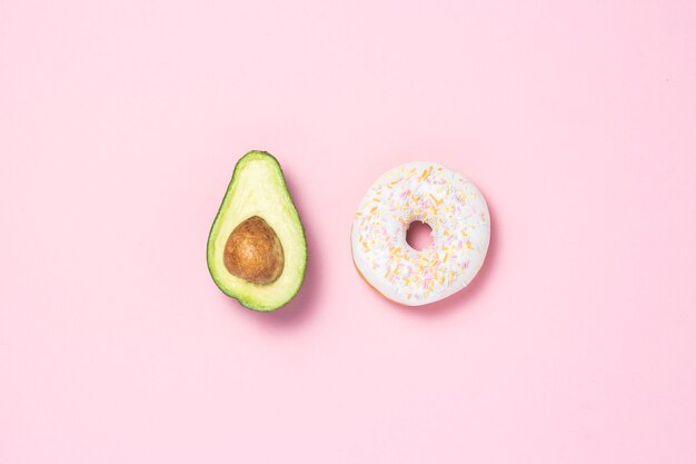 Medio aguacate y donut sobre un fondo rosa. Concepto de opciones de alimentos. Alimentos útiles o nocivos. Minimalismo Vista plana, vista superior.