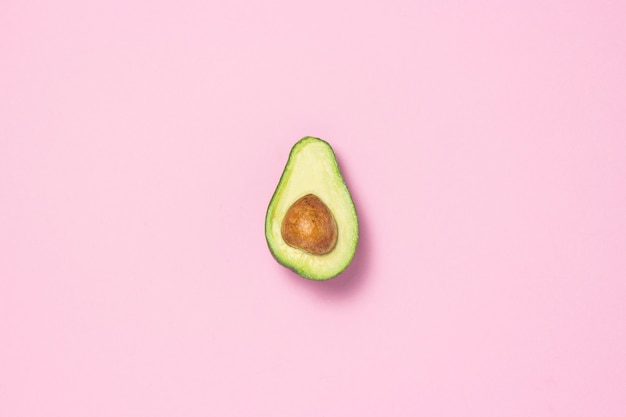 Medio aguacate sobre un fondo rosa. Concepto de alimentación saludable Vista plana, vista superior.