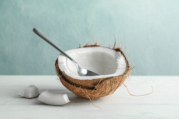 Medio coco con cuchara en mesa de madera contra gris