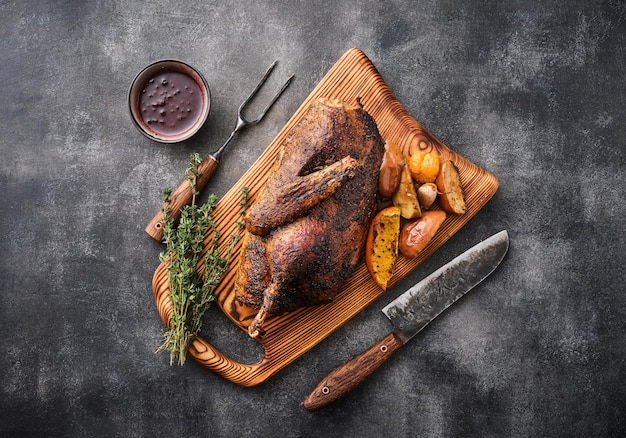 Medio ganso con salsa y manzanas al horno sobre una tabla de madera con cuchillo y tenedor sobre un fondo gris